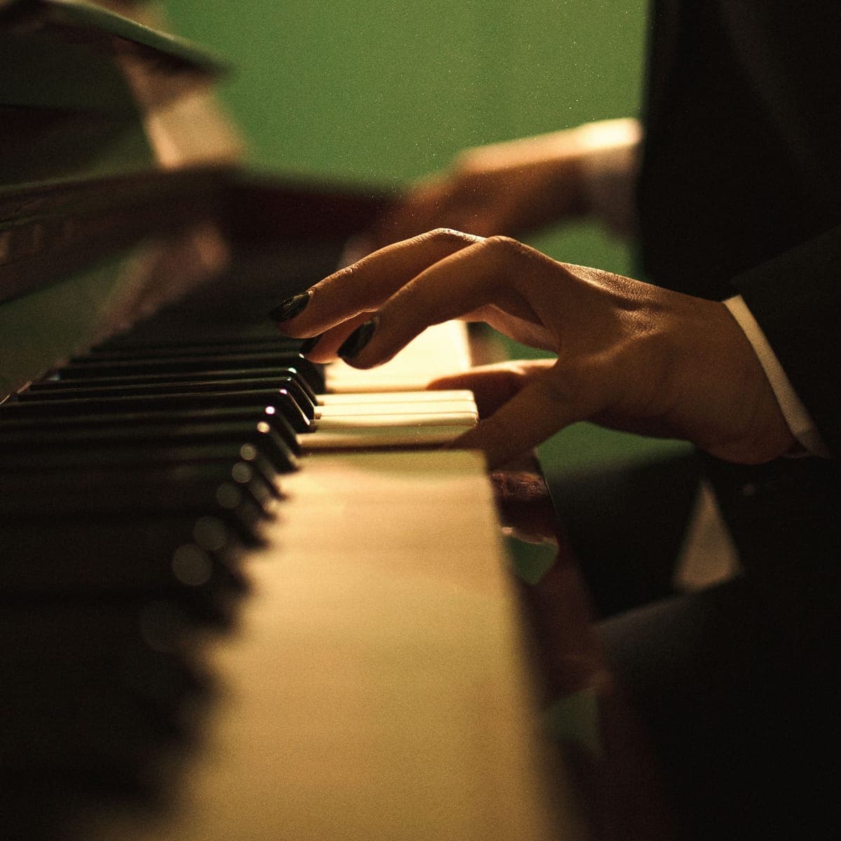 Hands on piano keys under warm stage light.