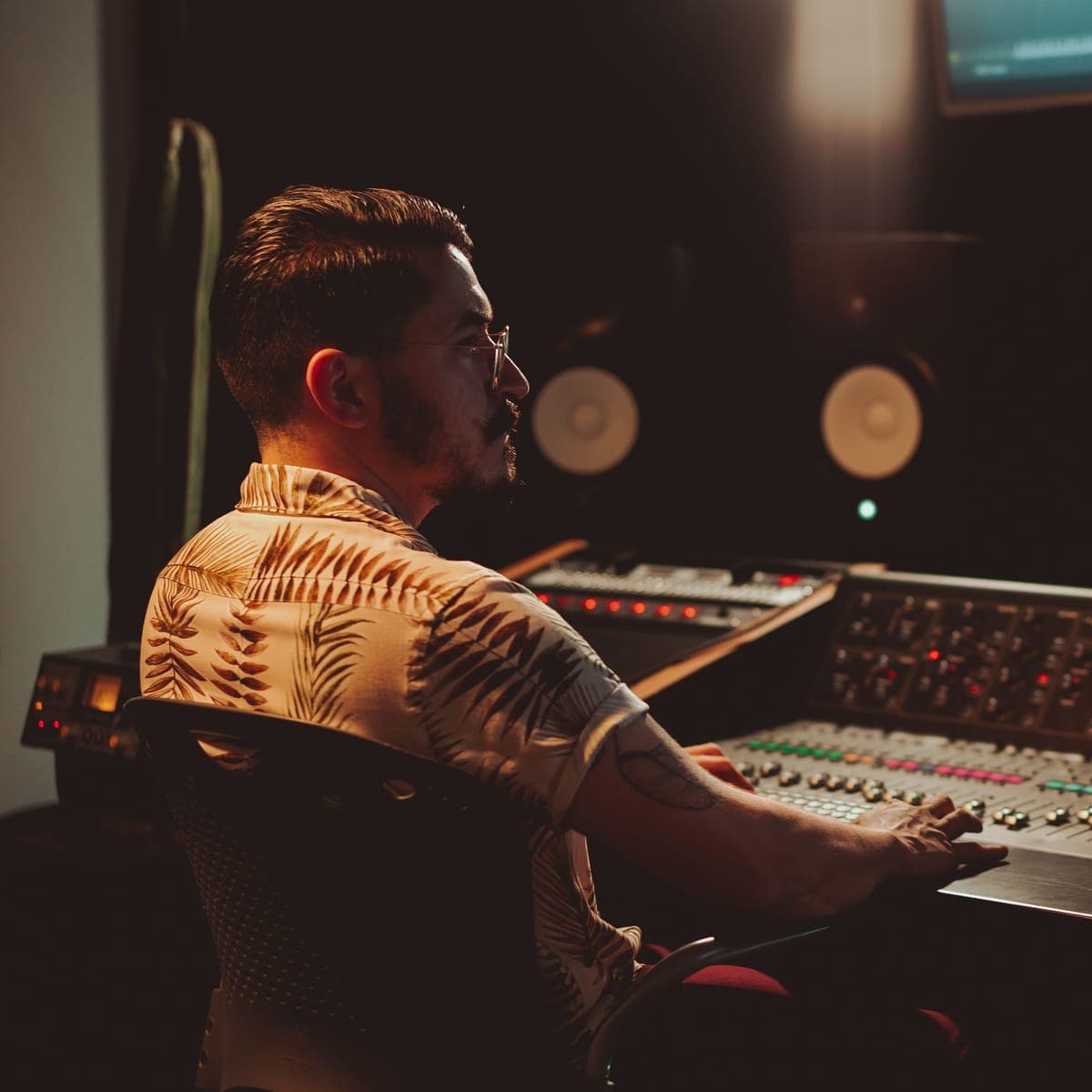An engineer at a mixing console in a dim control room.