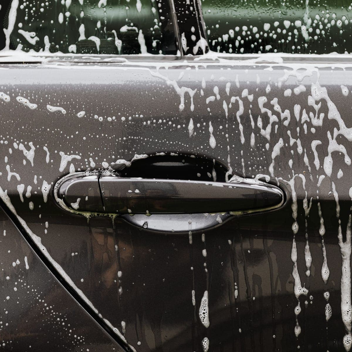 Snow foam running off a dark door panel during a wash.