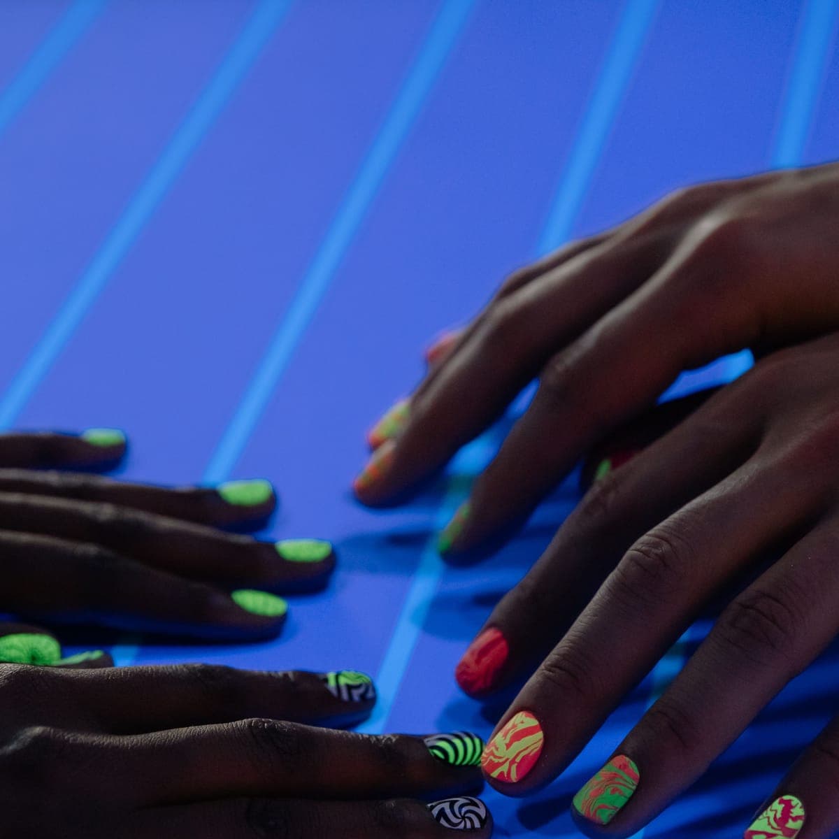 Neon nail art on a finished set of hands, lit blue.
