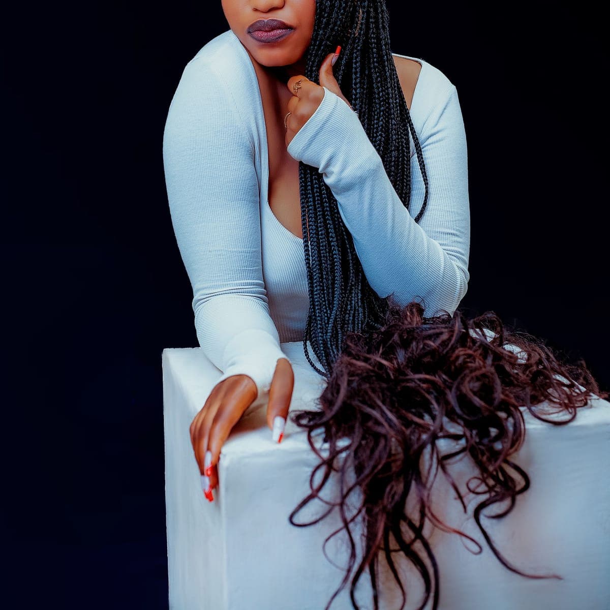 A client with long sleek knotless braids against a near-black backdrop.