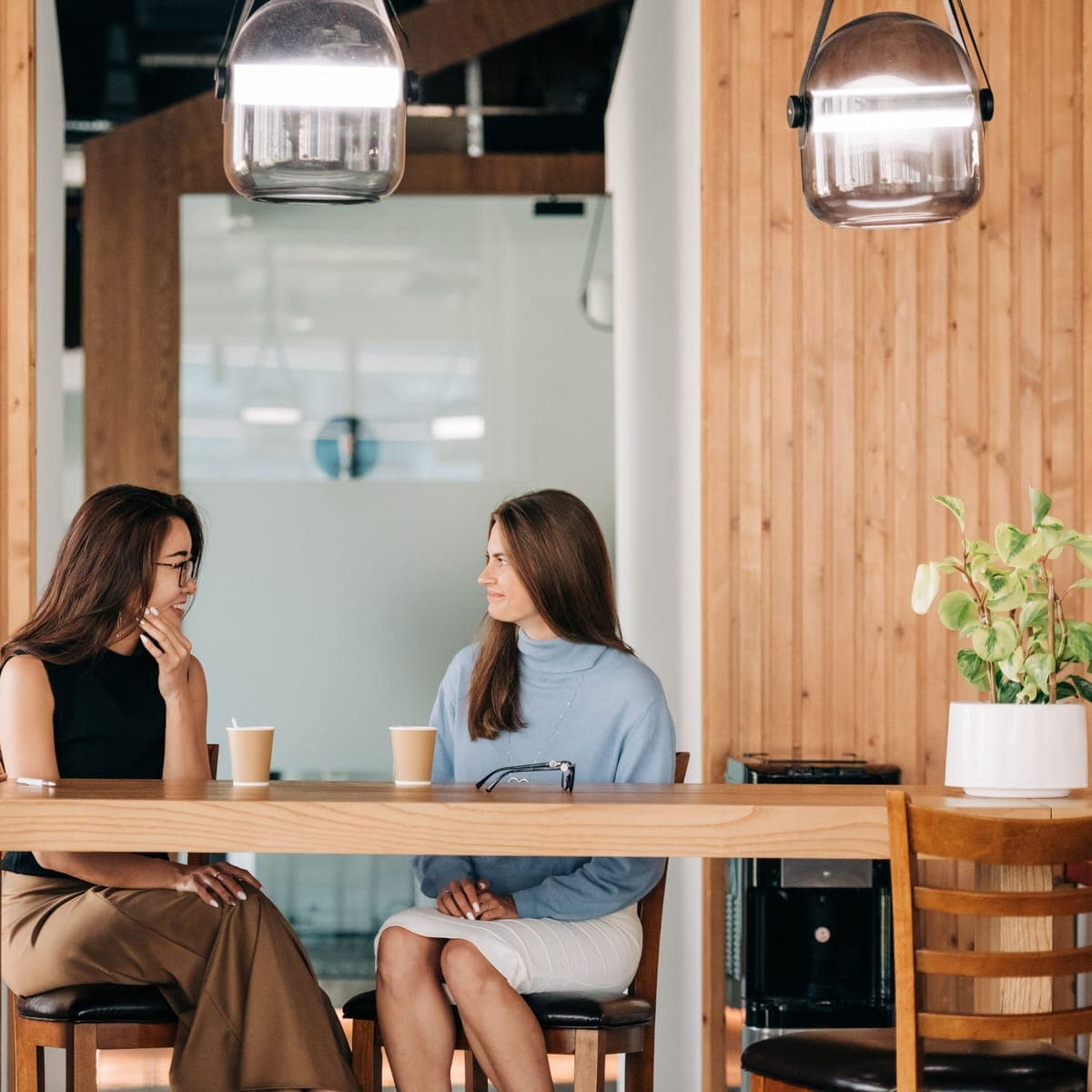 Two people talking over coffee at a counter in a bright cafe.