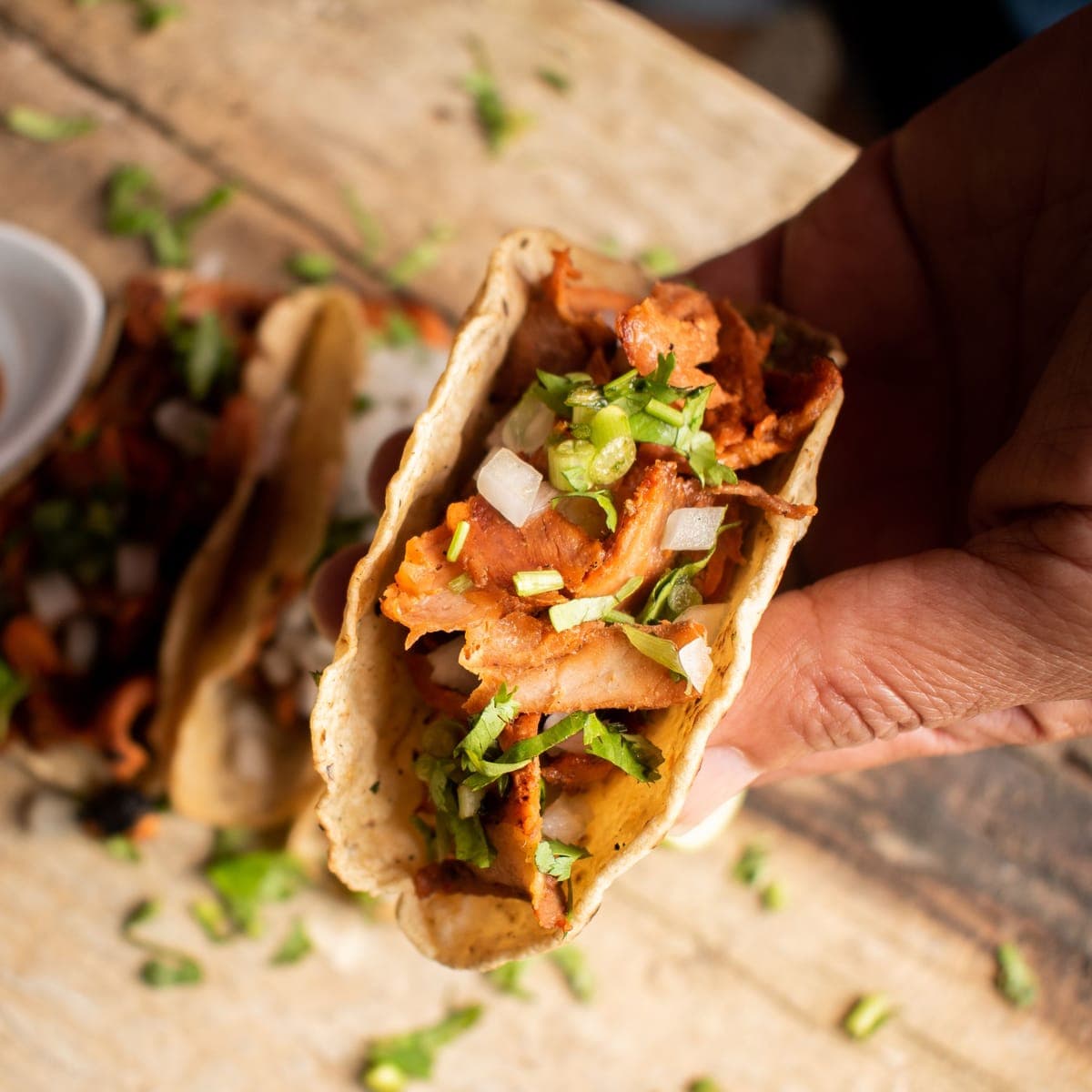 A hand holding one taco out toward the camera at the window.