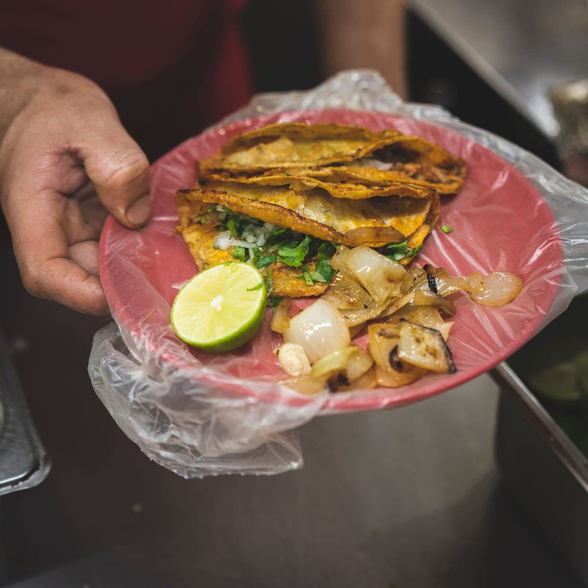A plate of golden fried tacos handed over with a lime.